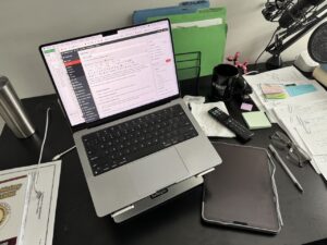 Laptop on a cluttered desk with documents and stationery